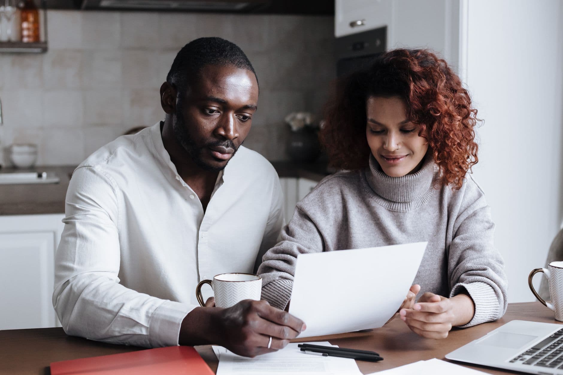 A couple sitting at a kitchen table reviewing financial paperwork while deciding whether to rent or buy a home