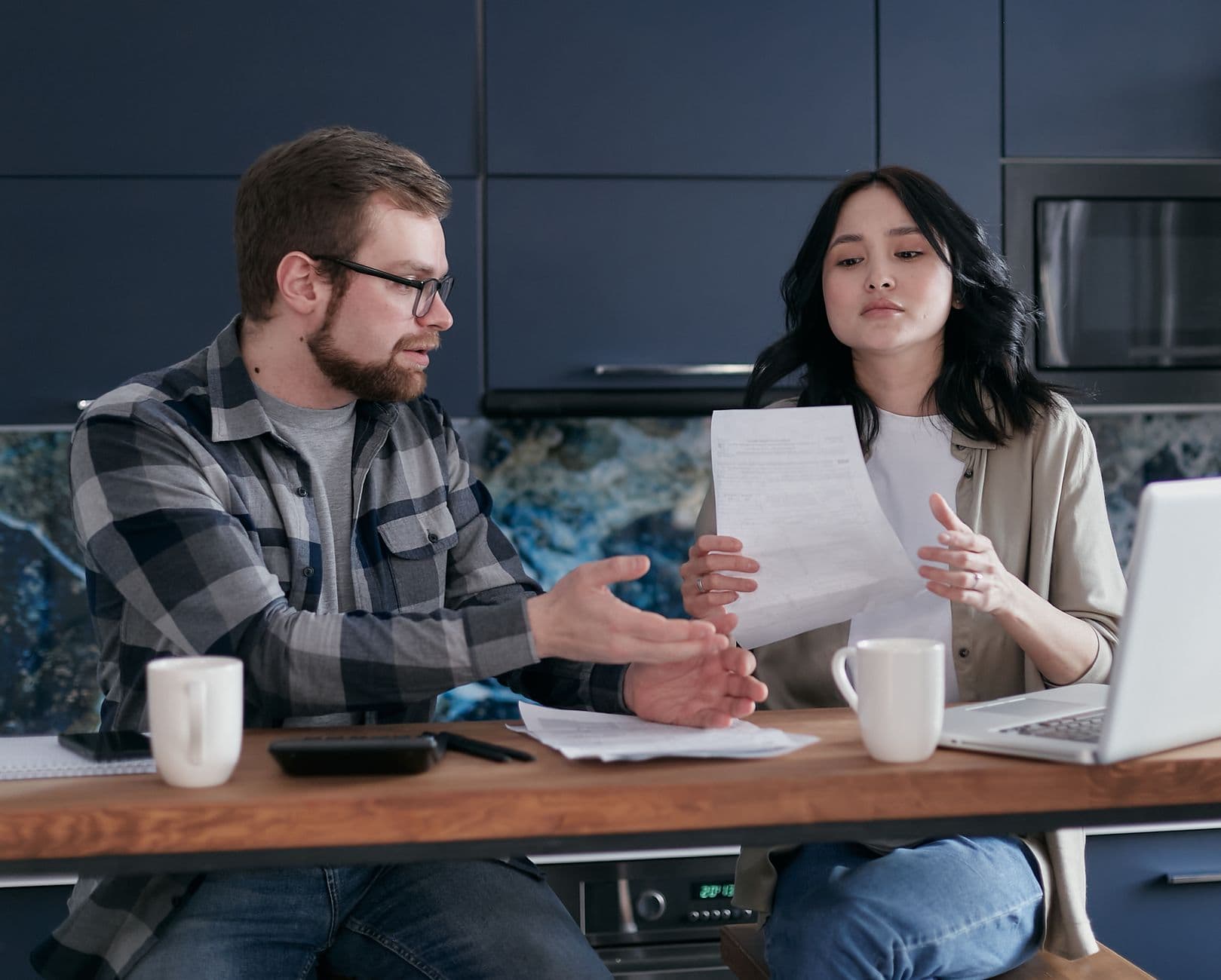 A small business owner reviewing monthly subscription statements on a laptop at a kitchen table